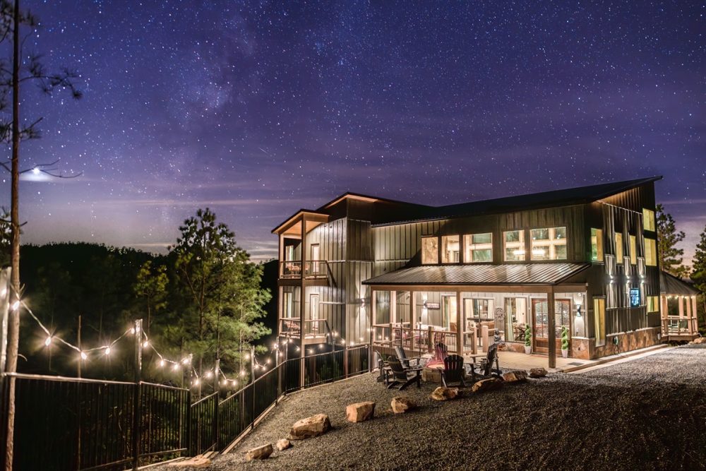 Large hillside cabin illuminated at night with outdoor string lights