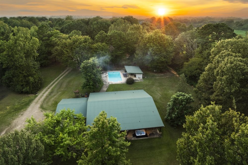 Aerial view of a cozy cabin with a green roof surrounded by trees, featuring