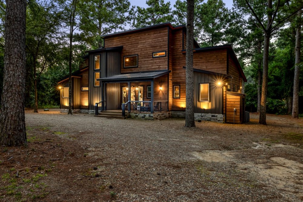 Luxurious cabin rental nestled amongst tall pine trees, showcasing a modern design with a wrap-around