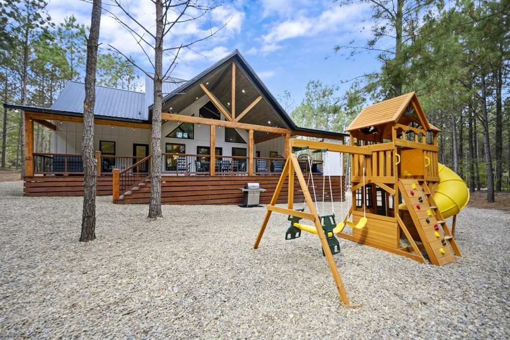 Cozy cabin exterior in a wooded area featuring a playground with swings and slide, ideal